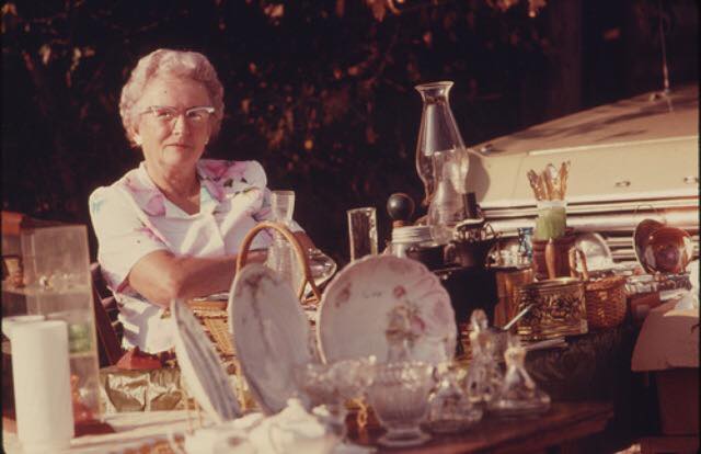 Image: Older woman at a table with vintage plates and sales